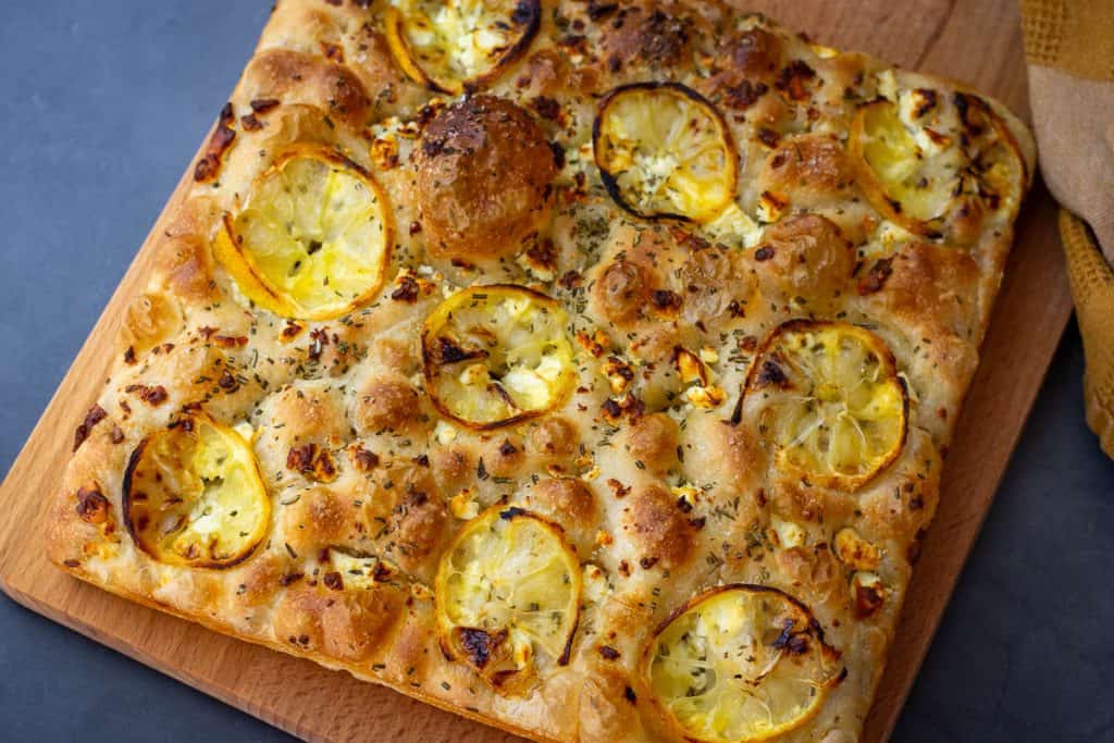 Baked lemon and feta focaccia on a wooden board.