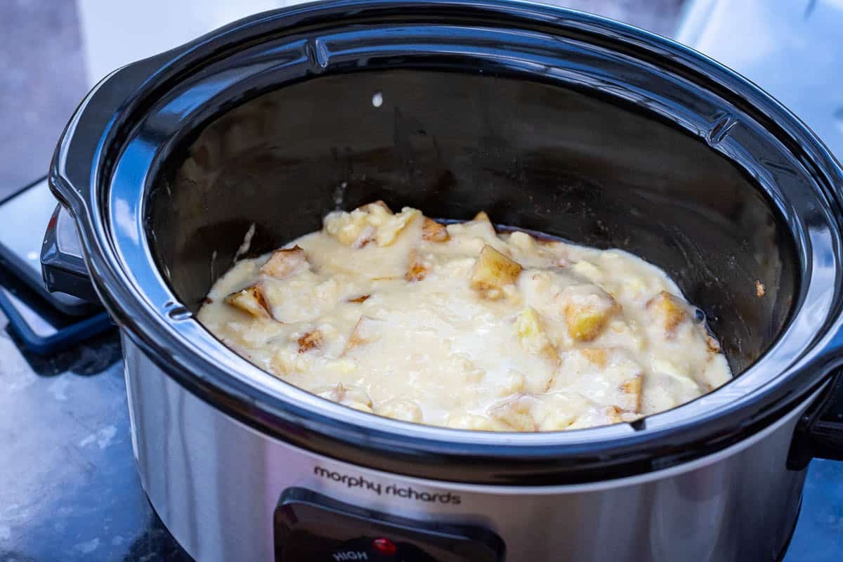 Sourdough discard cobbler batter poured over the apples in the slow cooker.