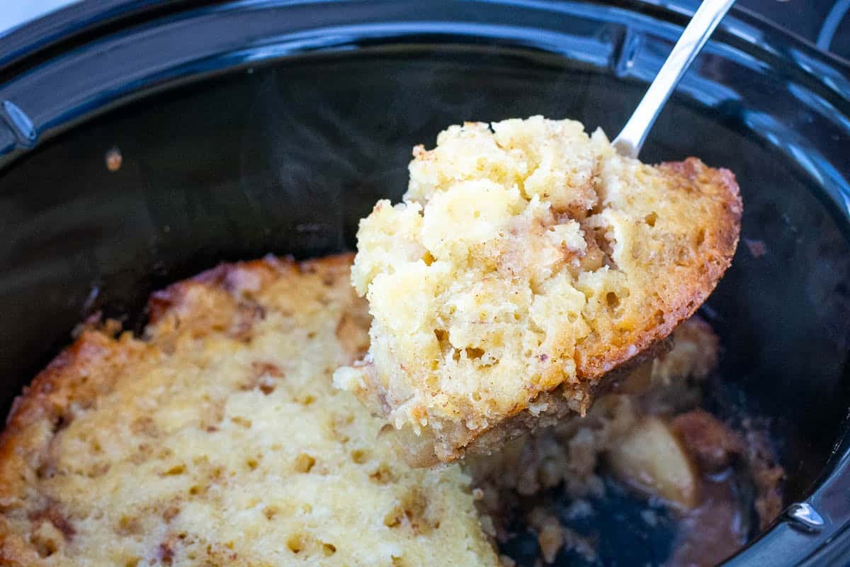 A portion of slow cooker apple cobbler being spooned out of of the slow cooker bowl.
