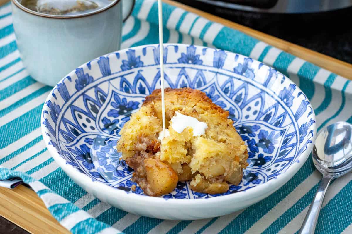 Delicious sourdough apple cobbler served in a blue and white bowl with whipped cream.