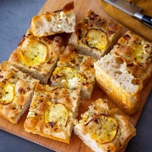Lemon and feta sourdough focaccia cut into squares on a wooden board.