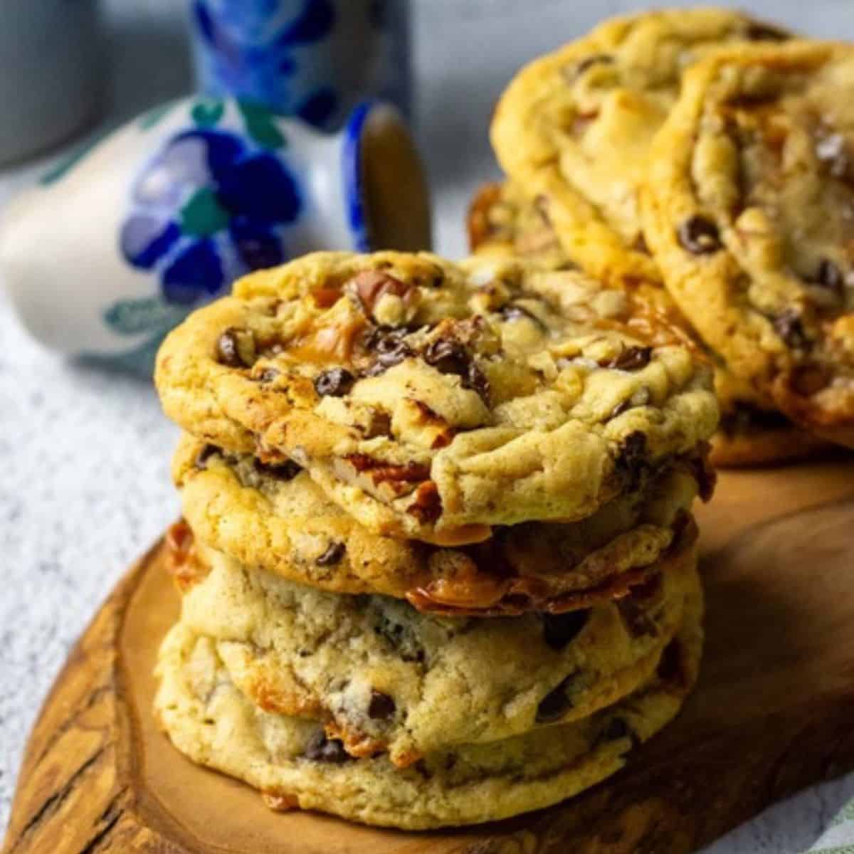 Stacks of sourdough turtle cookies packed with chocolate chips, pecans and caramel on a wooden board.