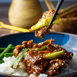 Slow cooker Mongolian pork piece being picked up from a bowlful.
