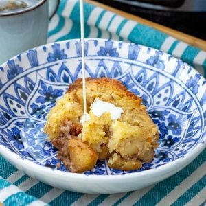 Cream being poured onto slow cooker sourdough apple cobbler in a blue bowl.