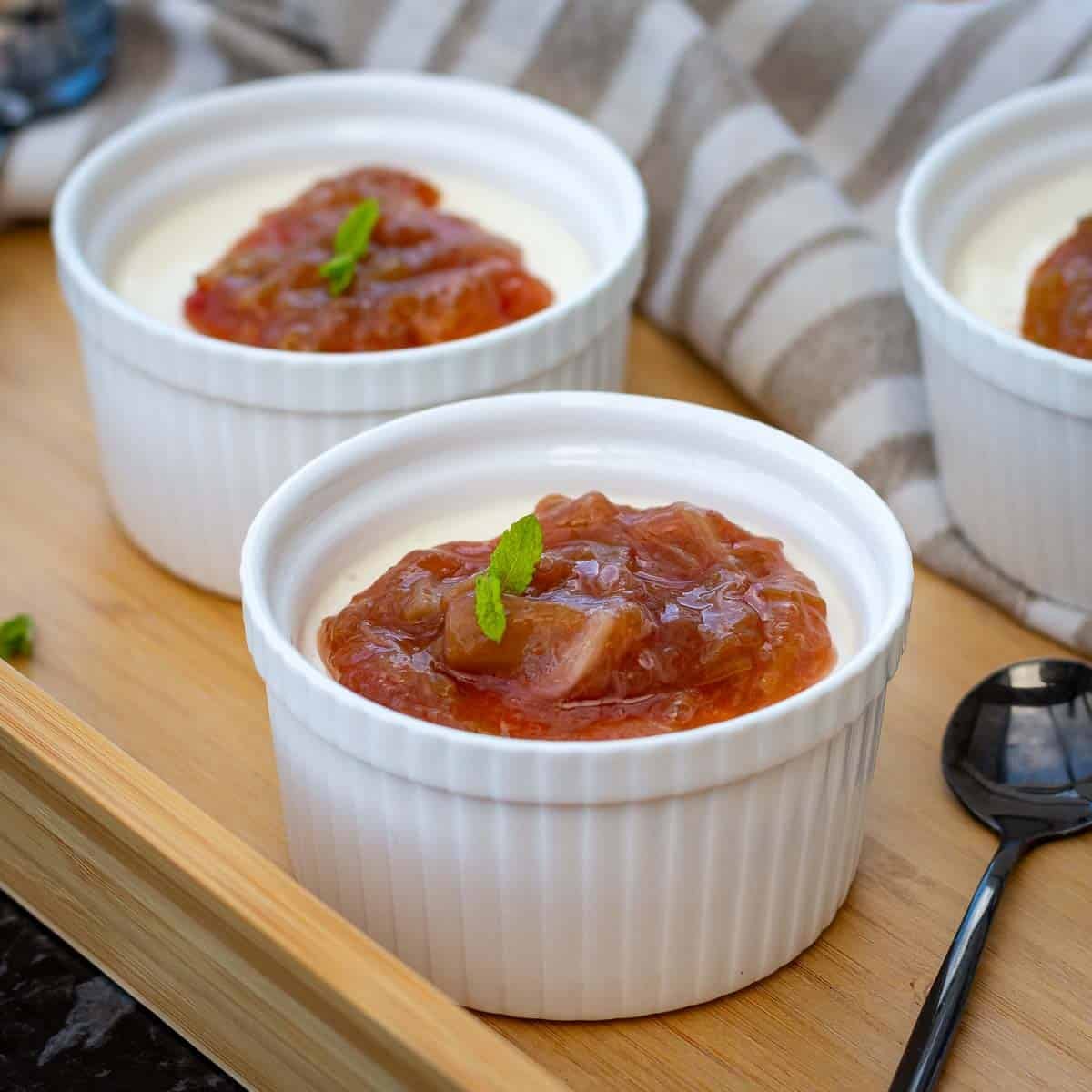 Kefir Panna Cotta with rhubarb compote set in white ramkins, garnished with mint.
