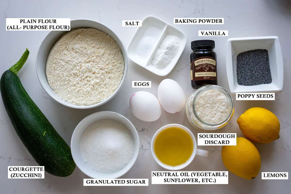 Labelled ingredients for Sourdough zuchhini muffins with lemon and poppy seeds on a light quartz worktop.