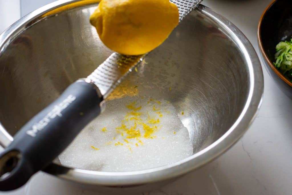 Zesting a lemon into a bowl of sugar using a microplane.
