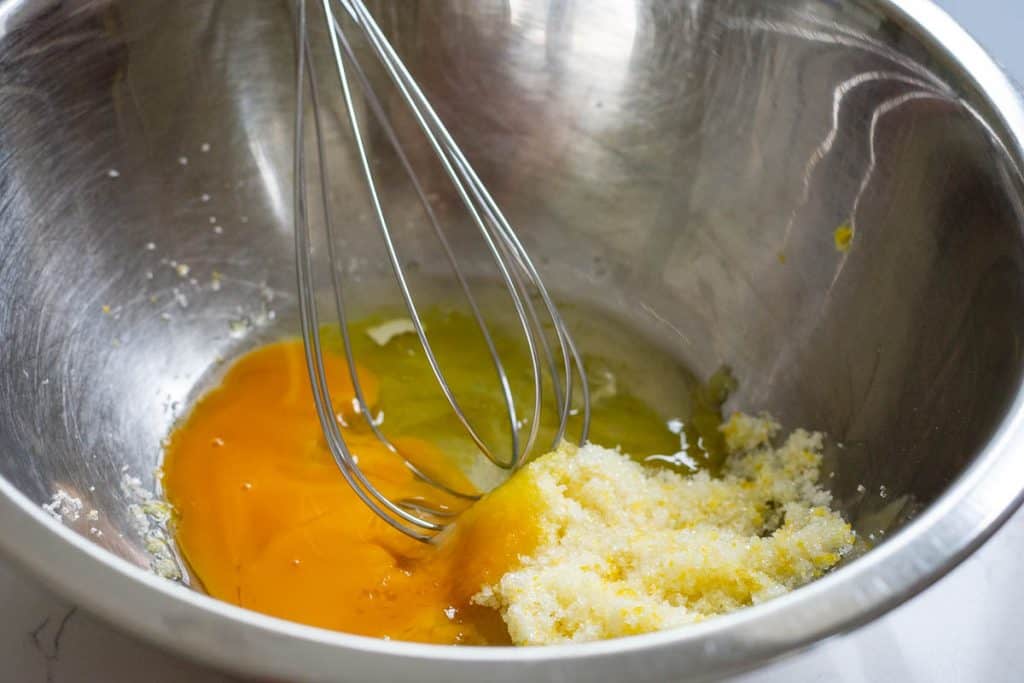 Whisking the eggs into the lemon sugar mixture in a mixing bowl.