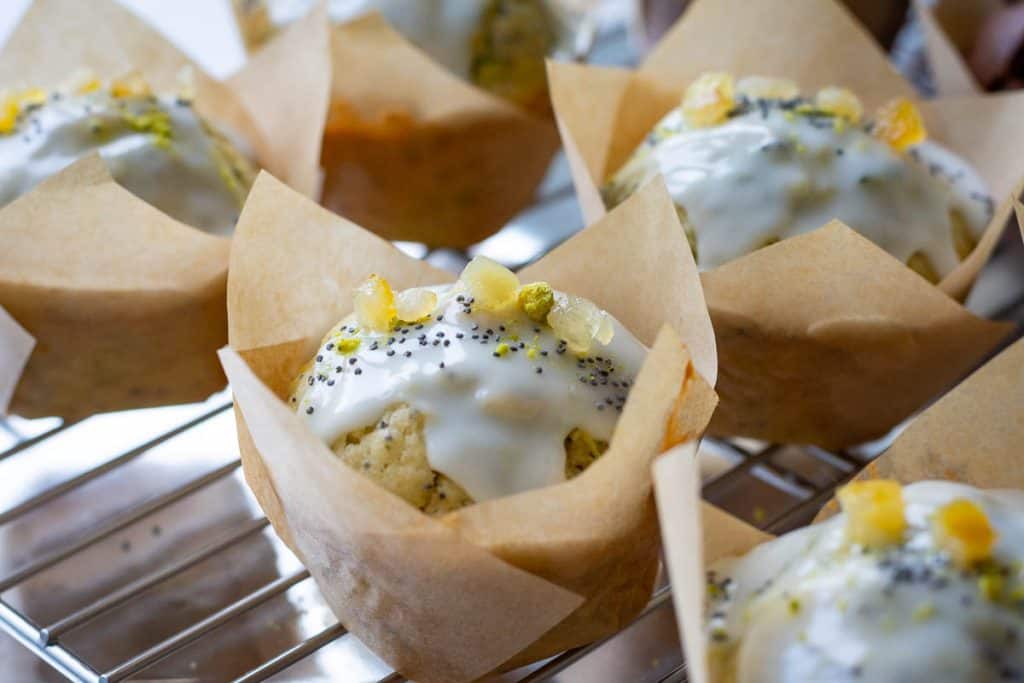 Sourdough courgette muffins on a wire rack with lemon glaze poured over the tops and decorated with a sprinkling of poppy seeds and candied lemon.