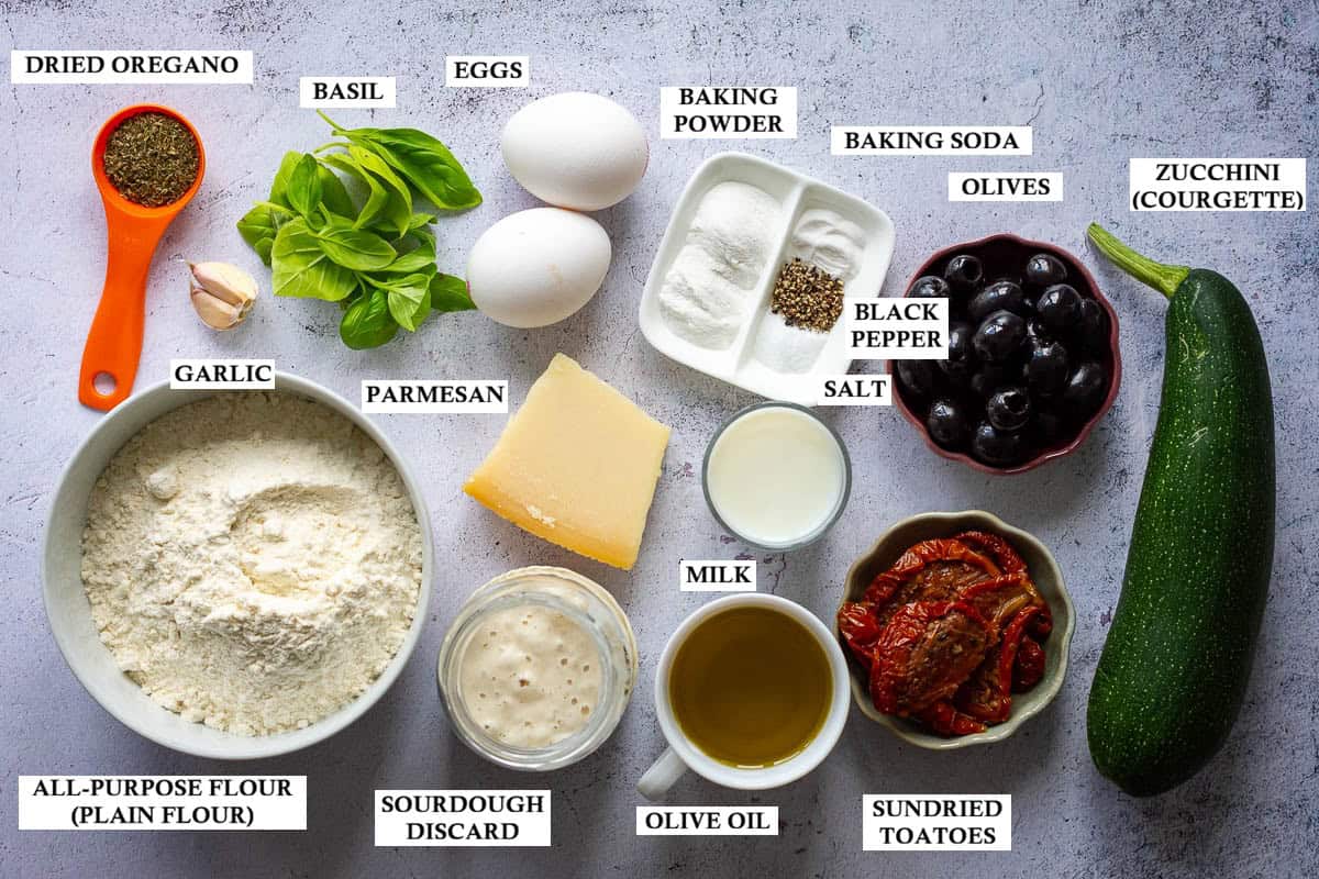 Labelled ingredients for Mediterranean style savoury sourdough discard zucchini bread on a light kitchen worktop.