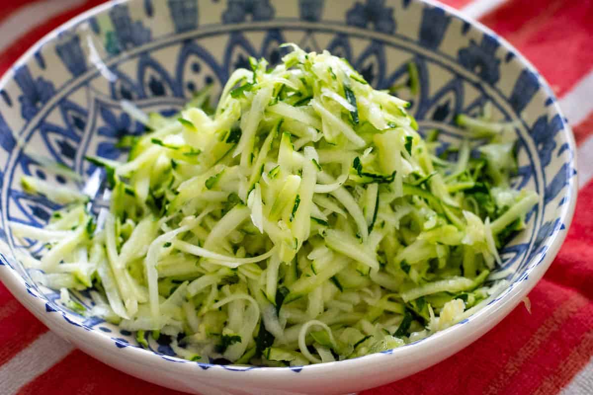 Coarsely grated courgettes in a decorative white and blue bowl.