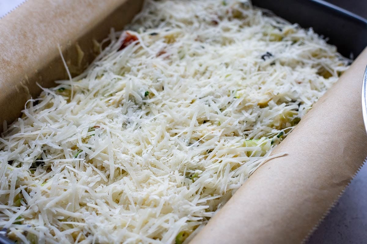 Sourdough courgette bread batter in a loaf pan with parmesan scaterred on top.