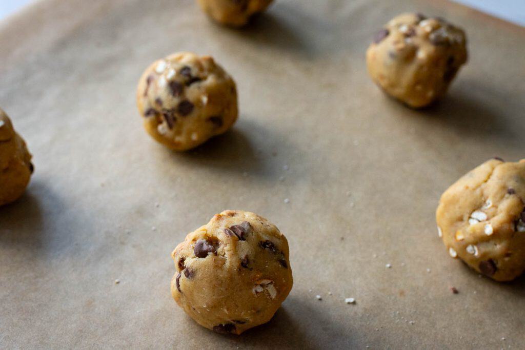 Sourdough choclate chip pretzel cookie dough balls spaced out on a baking sheet lined with parchment paper.