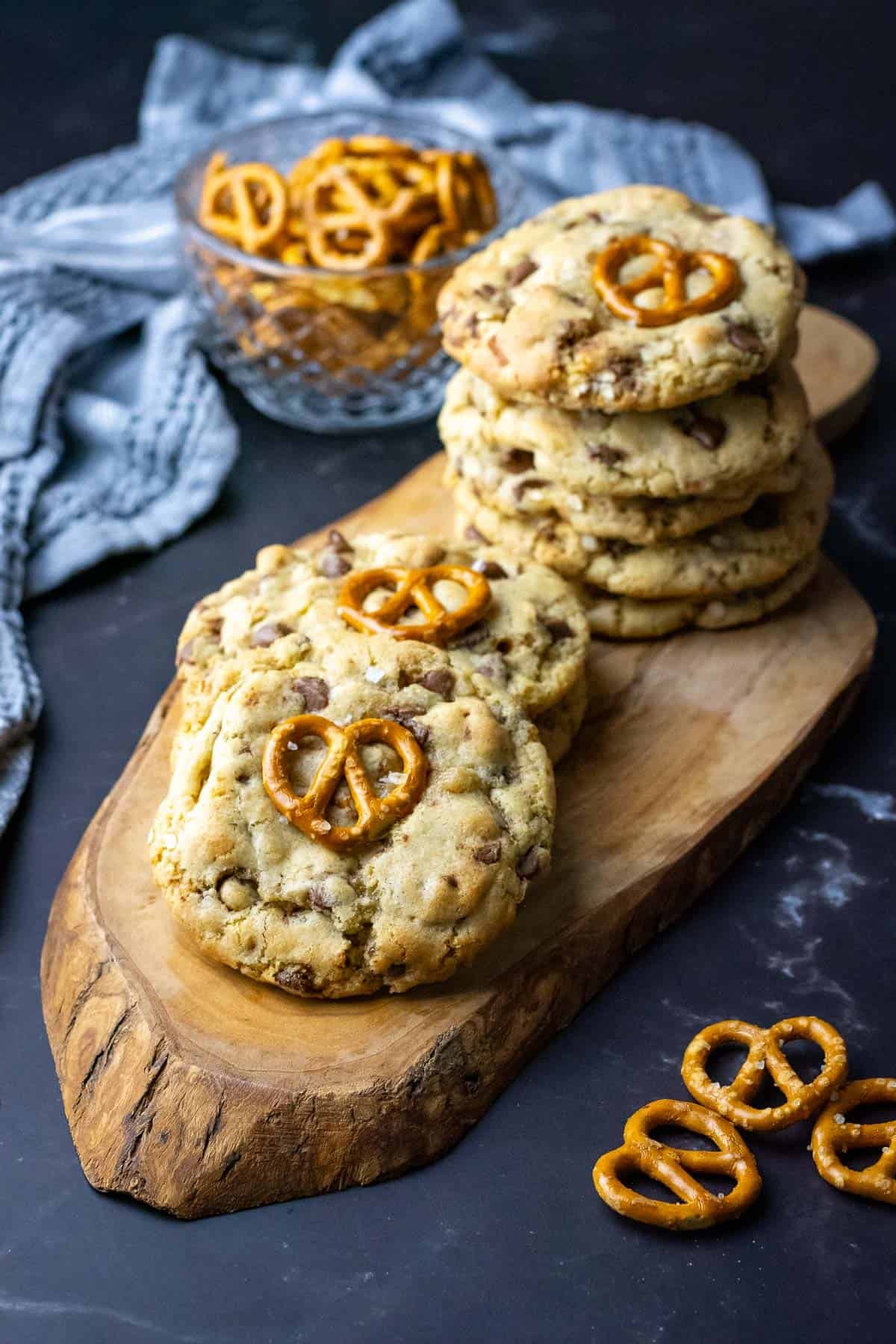 Stacks of sourdough chocolate chip pretzel cookies on a wooden board on a black surface.