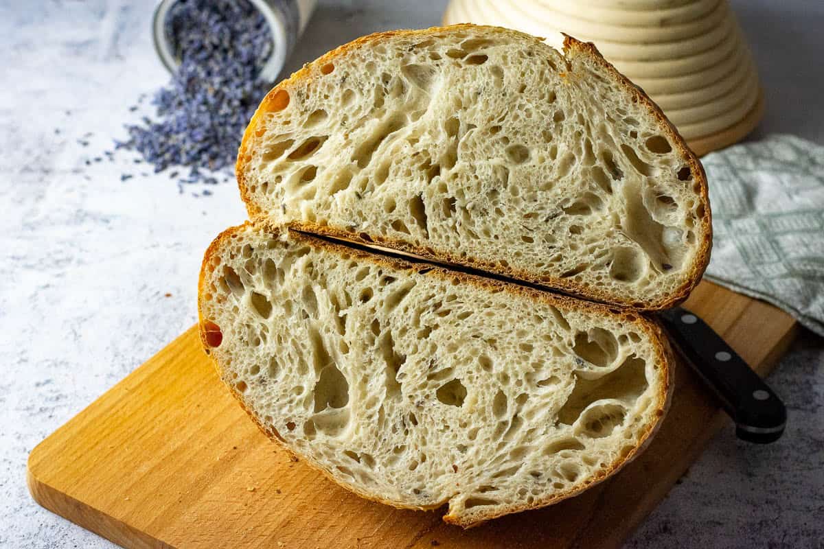 Honey and Lavender Sourdough Bread cut in half on a wooden board showing open crumb.