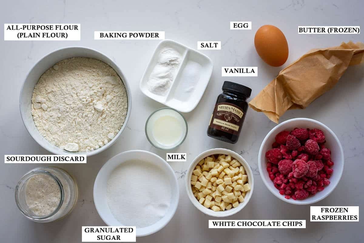 Labelled ingredients for sourdough scones with raspberries and white chocolate chips on a light quartz kitchen worktop.
