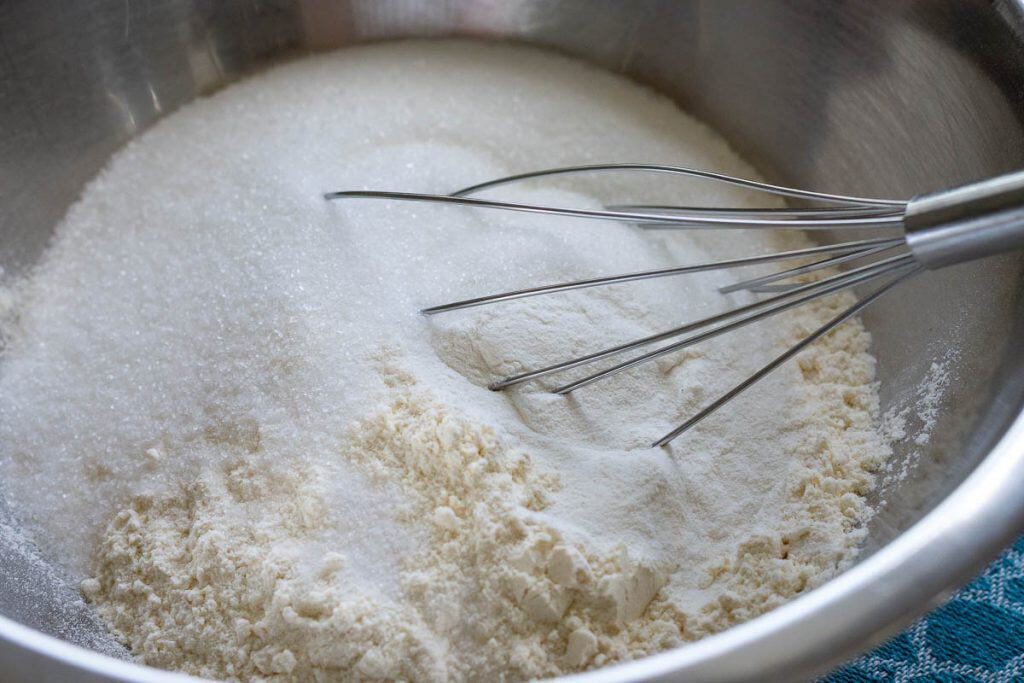 Mixing dry ingredients with a balloon whisk in a large meatl mixing bowl.