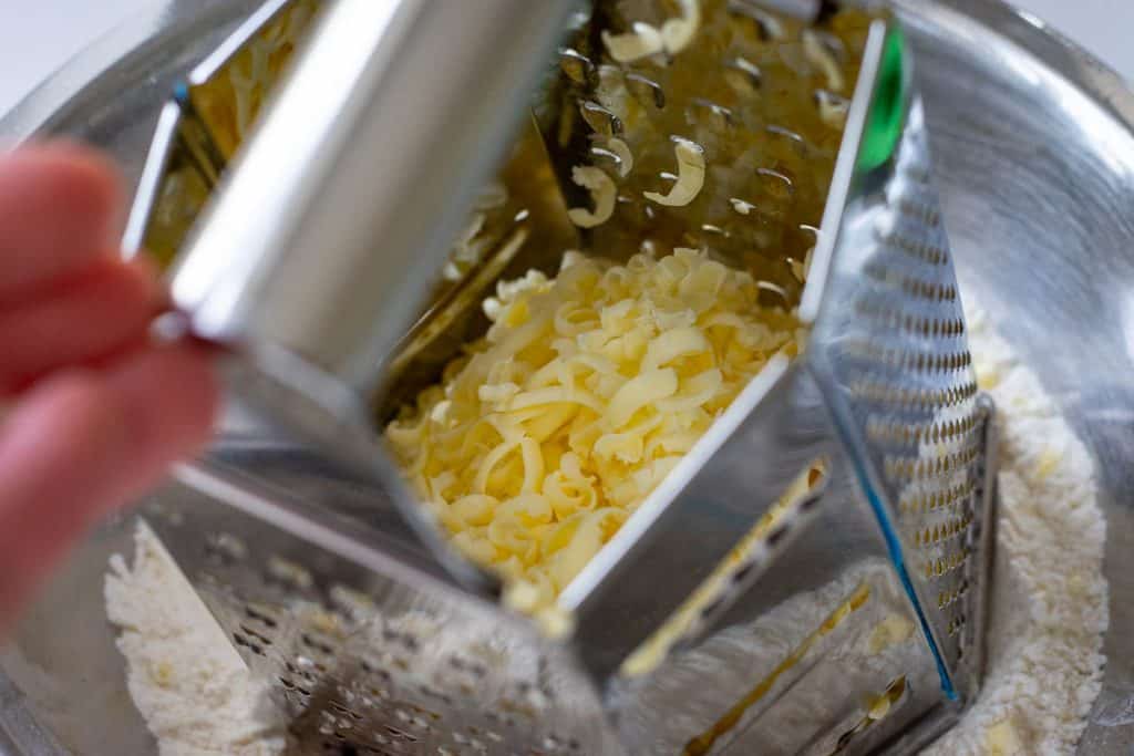 Grating frozen butter into the dry ingredients using a box grater.