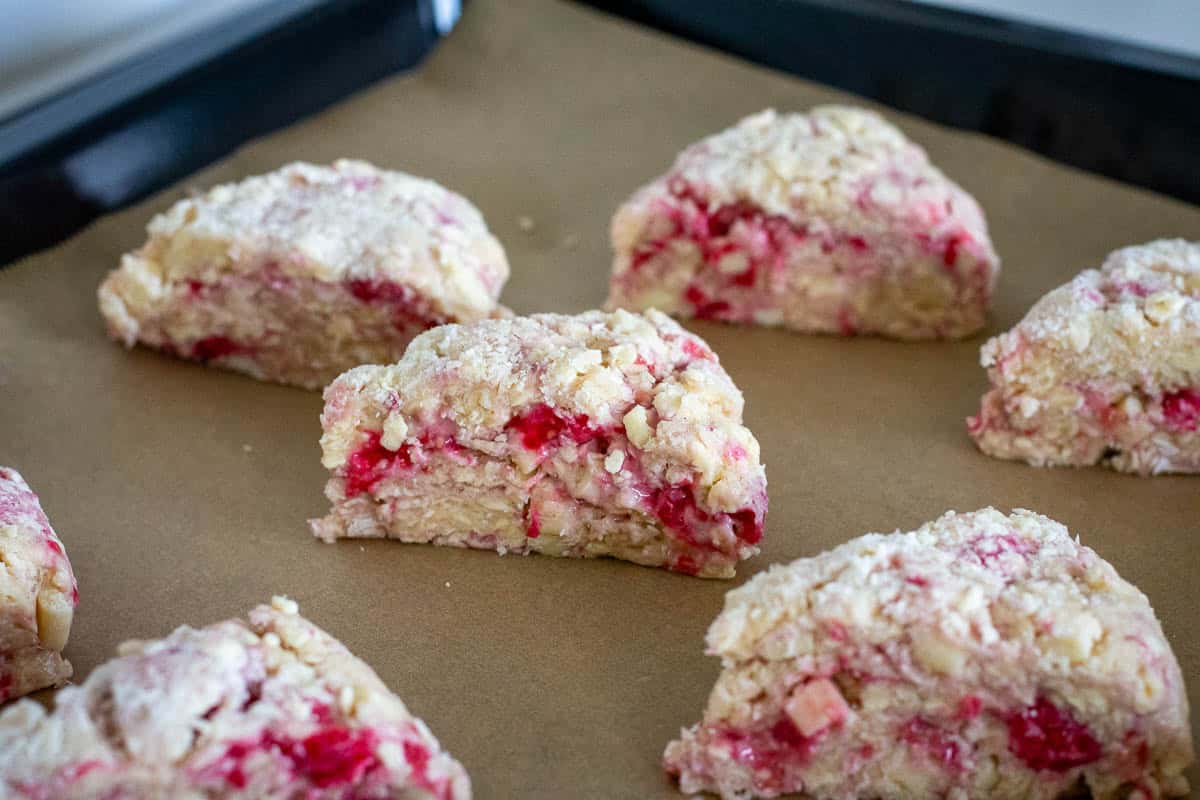 Raspberry and white chocolate sourdough scones arranged on a parchment paper lined baking sheet.