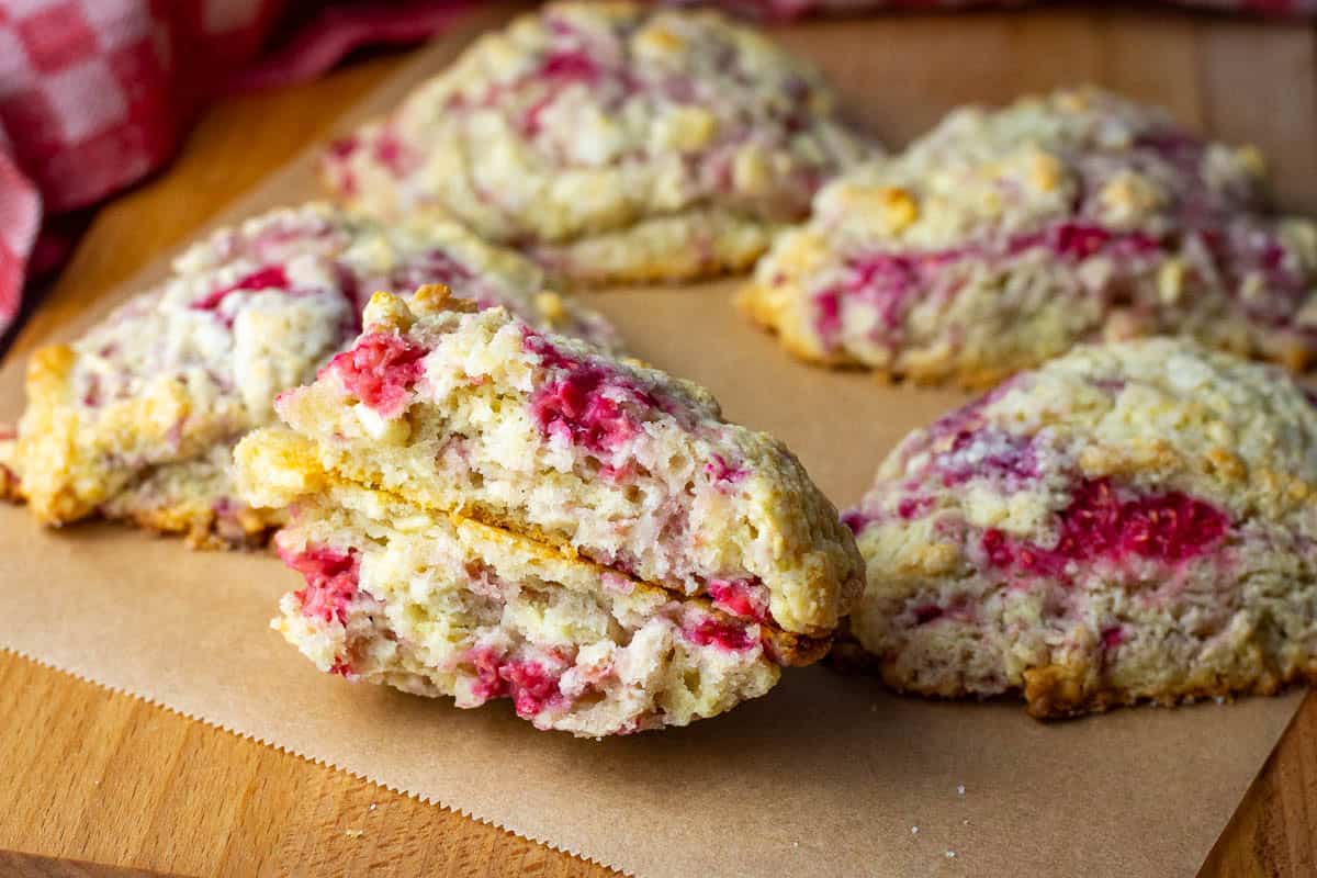 Raspberry and White Chocolate Sourdough Scones arranged on a wooden board with one broken in half exposing fruity chocolatey interior.