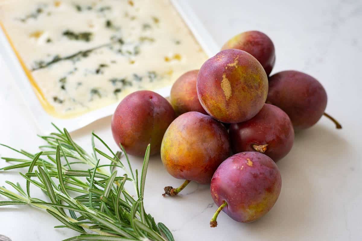 Plums, gorgonzola and rosemary on a light kitchen worktop.