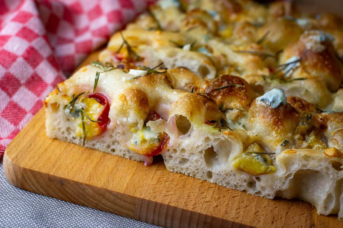A slice of gorgonozola and plum sourdough focaccia cut exposing airy crumb studded with plums and gorgonzola.
