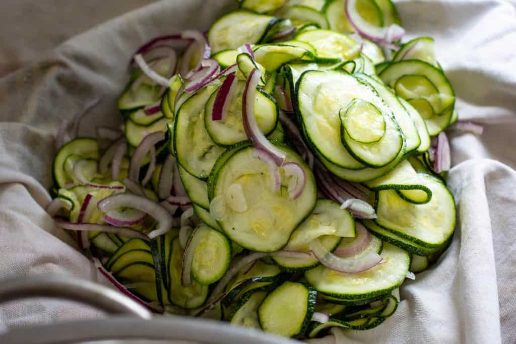 Salted zucchini and red onion in a clean kitchen towel.