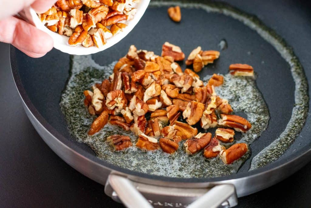 Adding chopped pecan nuts to melted butter in a frying pan.