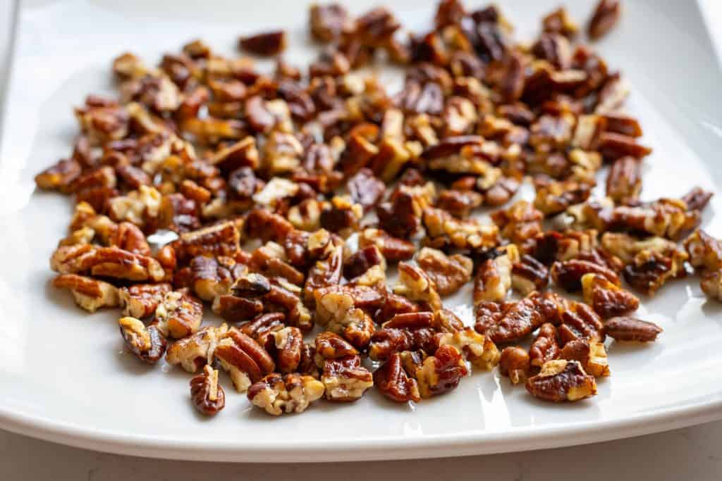 Toasted butter pecans cooling on a white plate.