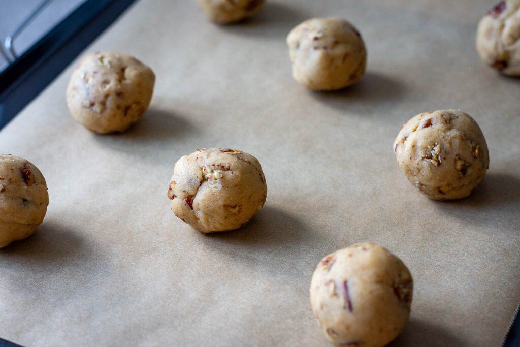 Balls of butter pecan sourdough cookie dough arranged on a baking sheet lined with parchment paper.