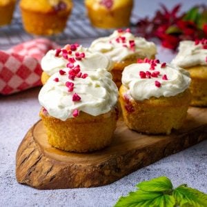 Sourdough Raspberry and White Chocolate Cupckaes with white chocolate cream cheese frosting arranged on a wooden board.