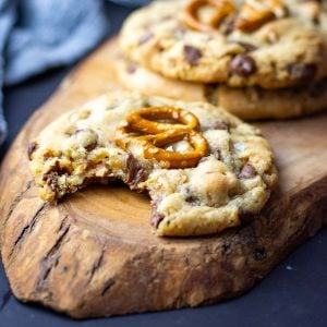 A bitten into sourdough chocolate chip and pretzel cookie on a decorative wooden board with more sourdough cookies in the background.