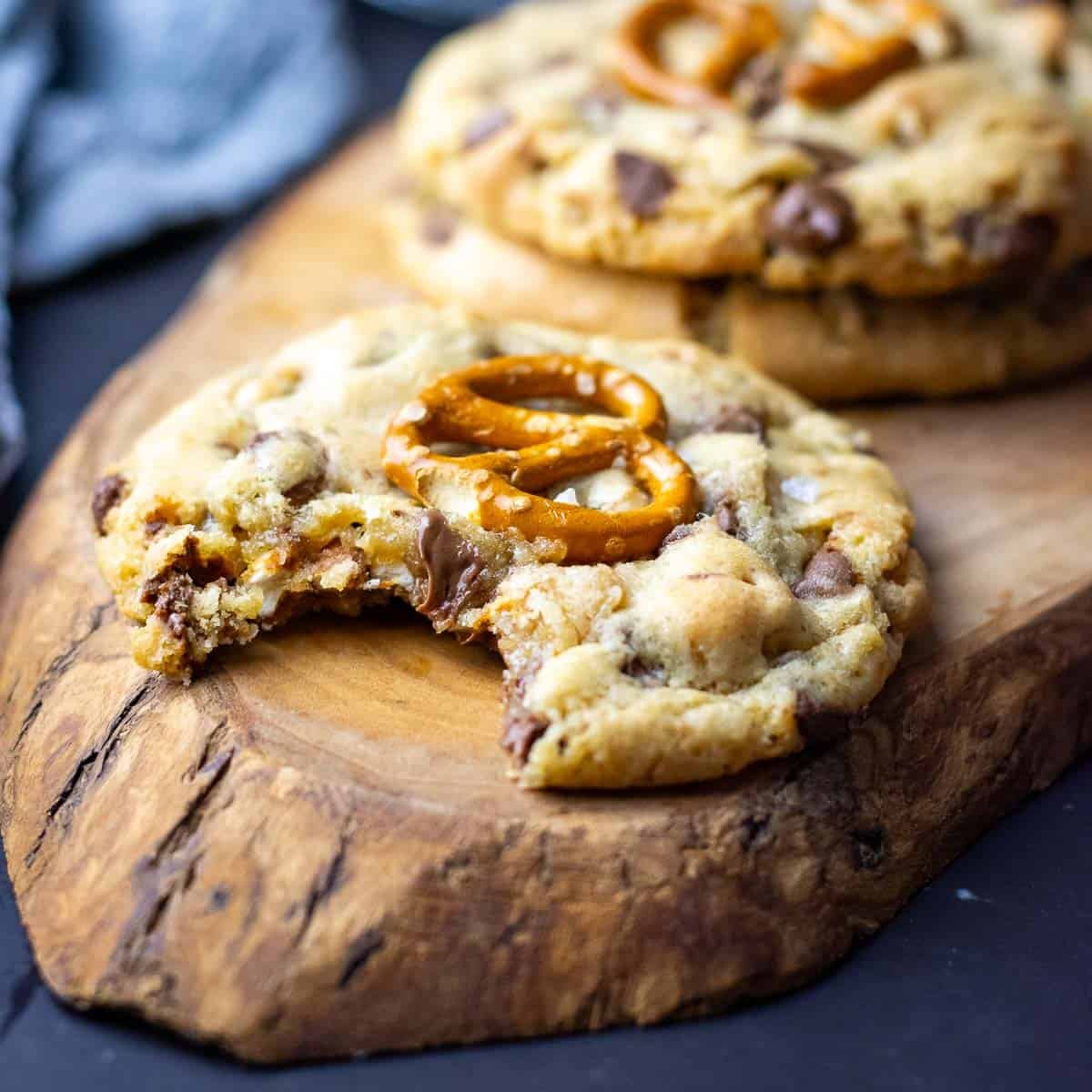 A bitten into sourdough chocolate chip and pretzel cookie on a decorative wooden board with more sourdough cookies in the background.