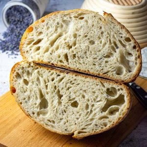 Honey and Lavender Sourdough Bread cut in half on a wooden board showing open crumb.