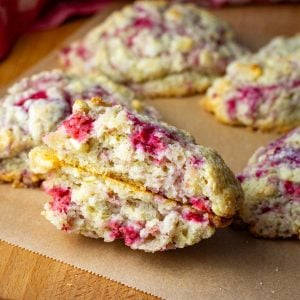 Raspberry and White Chocolate Sourdough Scones arranged on a wooden board with one broken in half exposing fruity chocolatey interior.