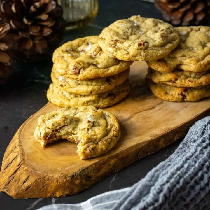 Stacks of butter pacan sourdough cookies on a decorative wooden board with one sourdough cookie already bitten into.