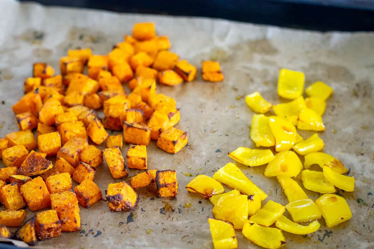 Roasted butternut squash on one side of a baking sheet and bell peppers on the other.