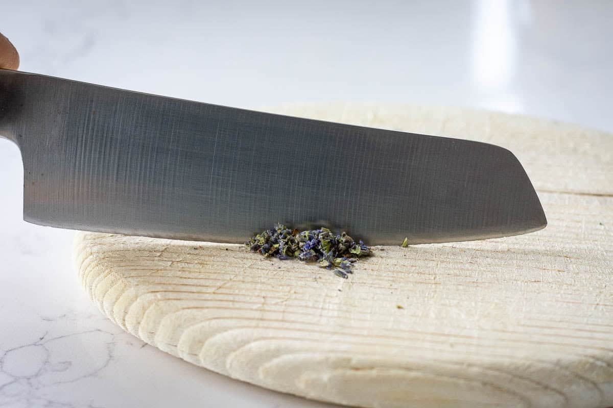 Finely chopping culinary lavender on a wooden board.