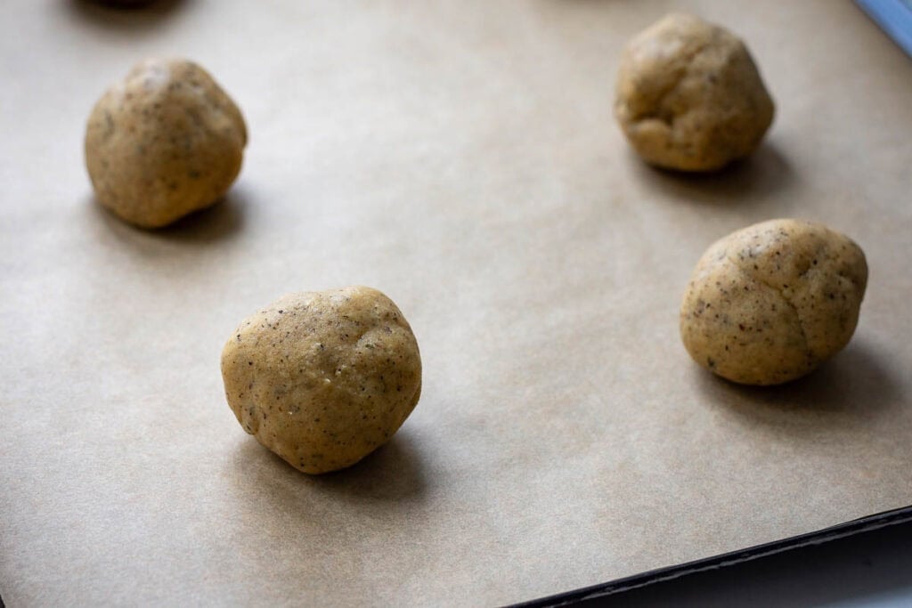 Six sourdough discard cookie dough balls on a parchment paper lined baking sheet.