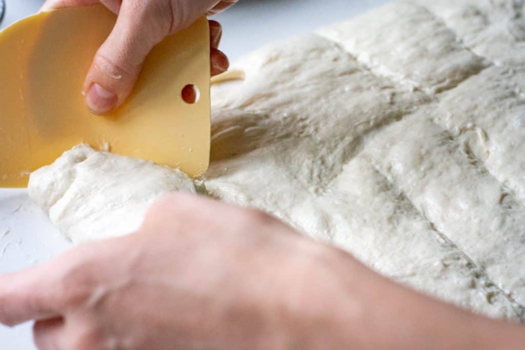 Dividing sourdough focaccia dough into 12 pieces on a light kitchen worktop.