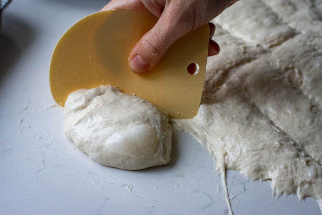 Shaping a sourdough focaccia muffin with a flexible bench scraper.
