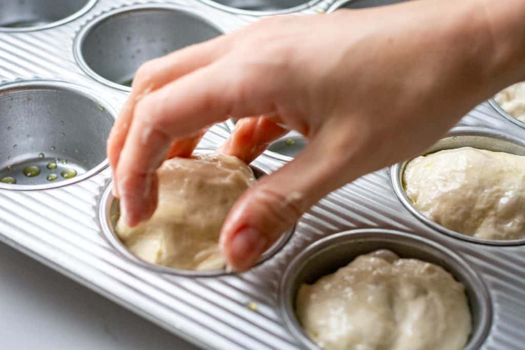 Placing sourdough focaccia muffin in an oiled muffin tin.
