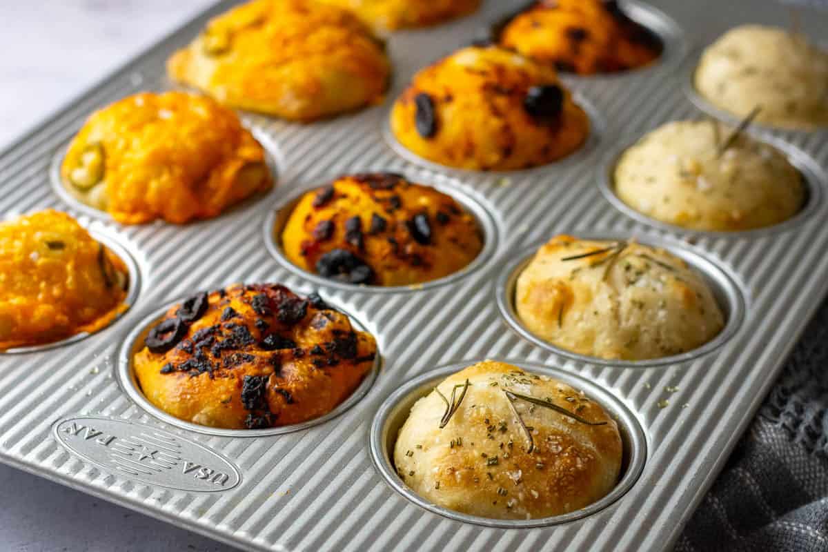 Baked sourdough focaccia muffins resting in a muffin pan.