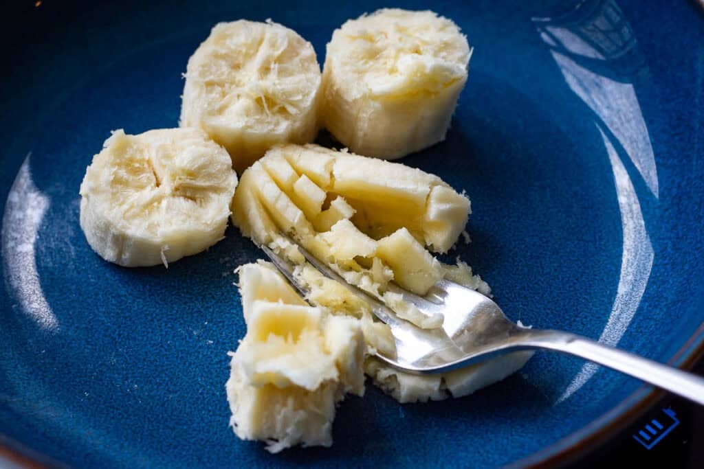 Ripe banana being mashed with a fork in a blue bowl.