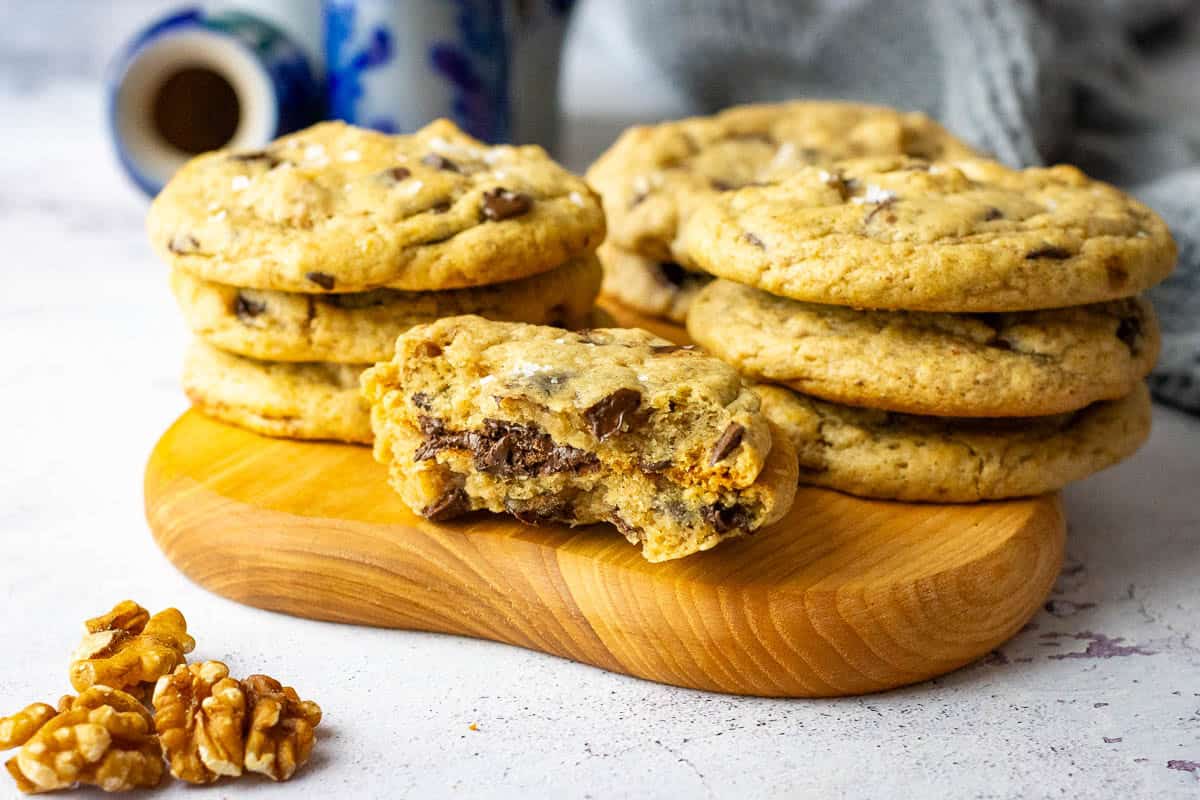 Stacks of sourdough banana bread cookies with one of the sourdough cookies broked in half exposing walnut and chocolate chip studded interior.