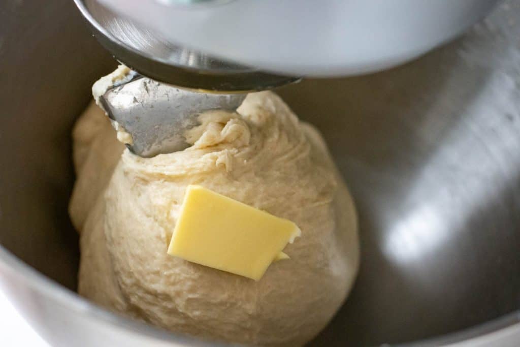 Softened butter gradually being added to the running mixer with the sourdough in it.