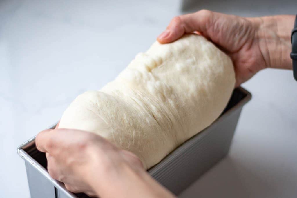 Placing shaped sourdough pyllman loaf into a pullman pan for second rise.