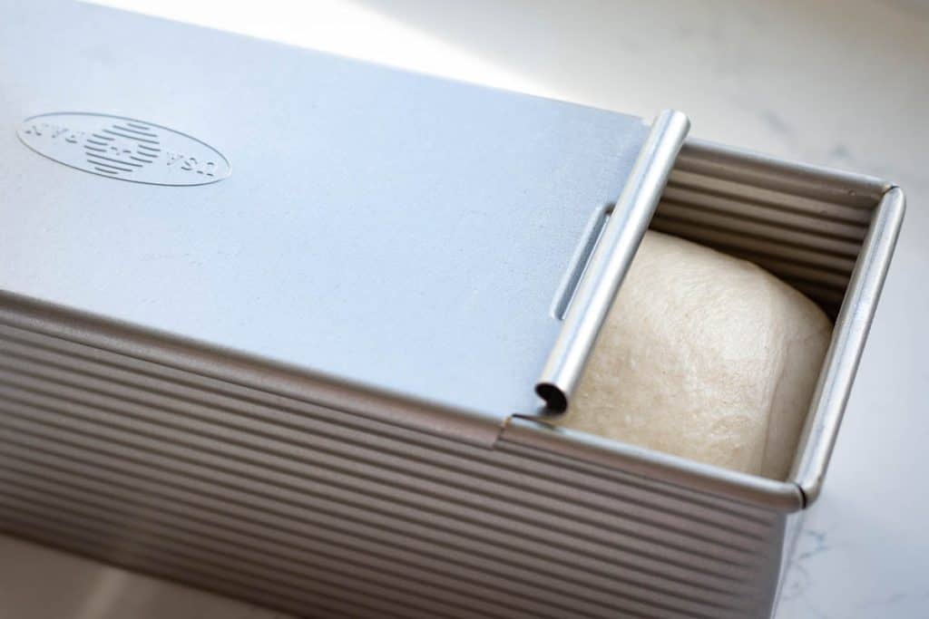 The lid being slid onto a pullman pan.