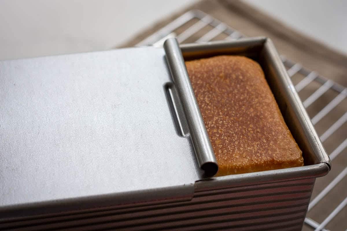 The lid being slid off the pullman pan exposing golden brown sourdough pain de mie.