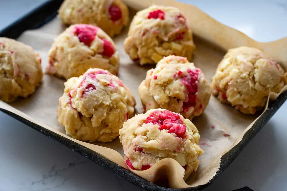 Raspberry and white chocolate sourdough cookie dough balls on a parchment paper lined baking sheet ready for freezing.